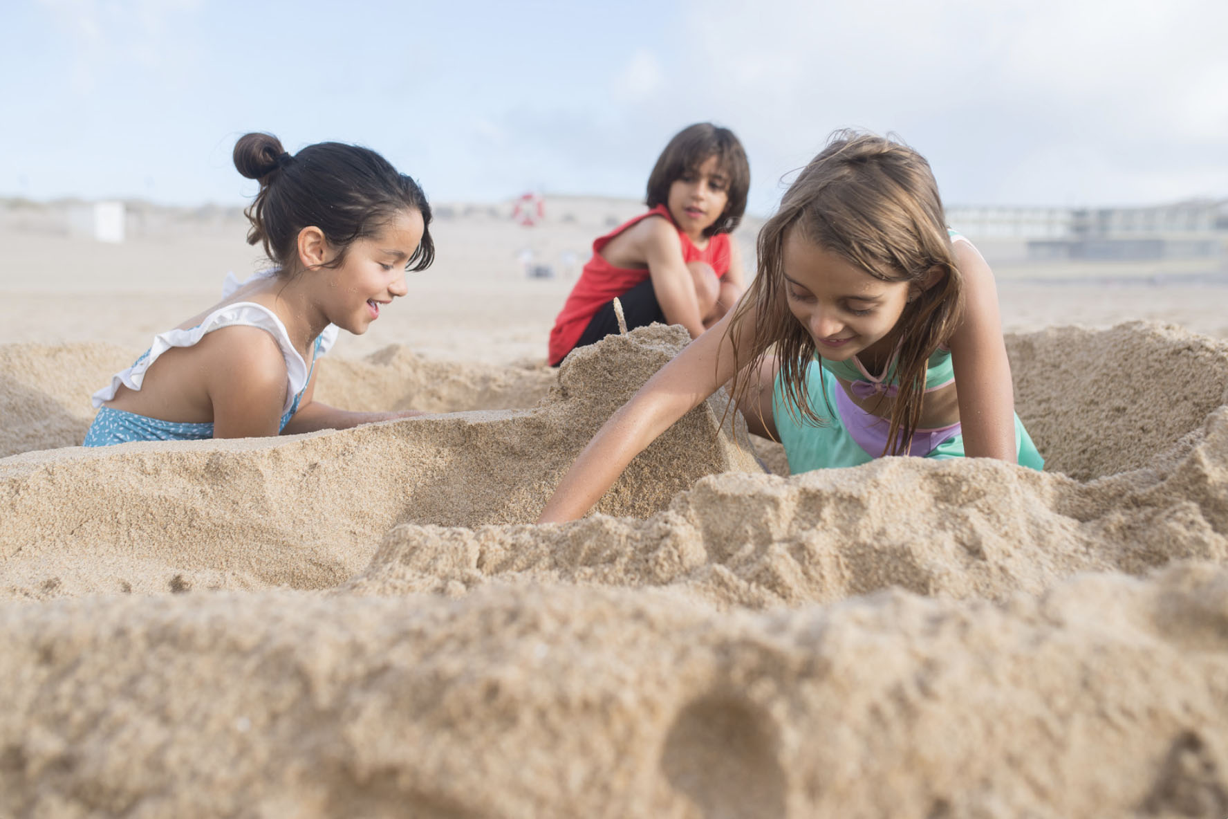Three children at the beach, digging and playing in the sand