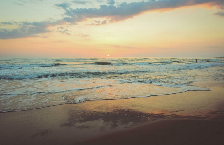 Dusty calm sunset over the beach with people in the small waves.