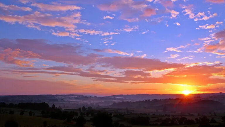 Bright orange sunset with low lush horizon and blue sky.
