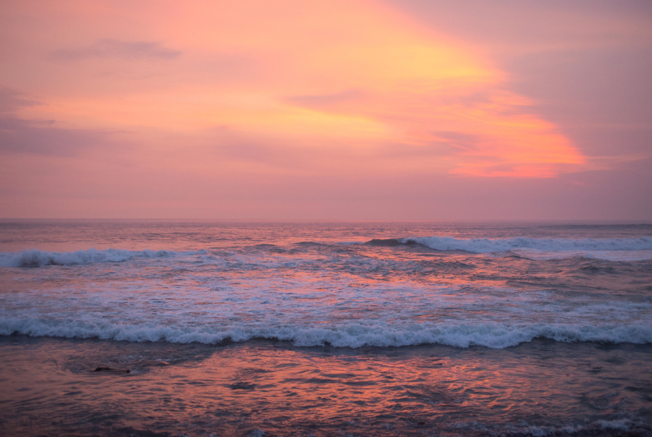 Pink sky over ocean with white cap waves.