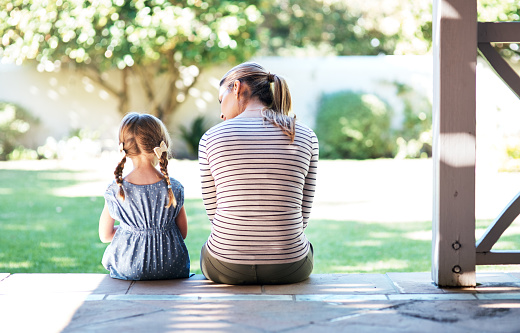 Mom and daughter facing out toward yard on porch step. Discussion. Bright day.