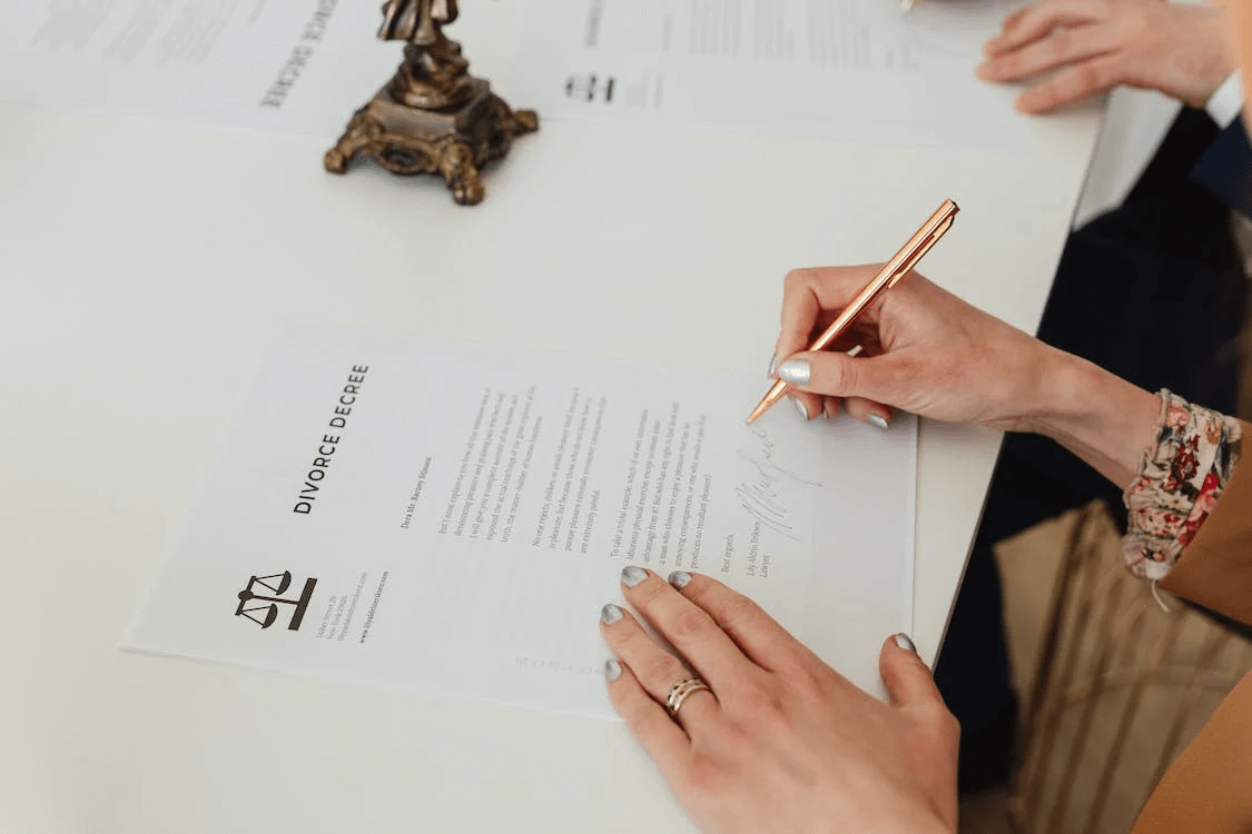 woman's hands using gold pen, signing document that says the words divorce decree.
