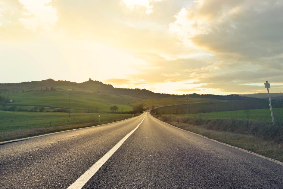 Highway that goes far into the distance with lush green landscape and bright sky.