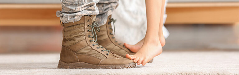 Cilds feet standing on the toes of the parents army boots.