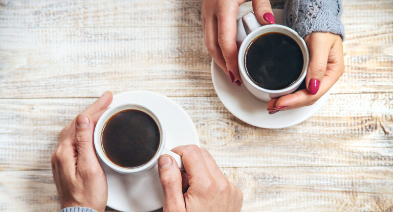 man and woman's hands around cups of coffee on table.
