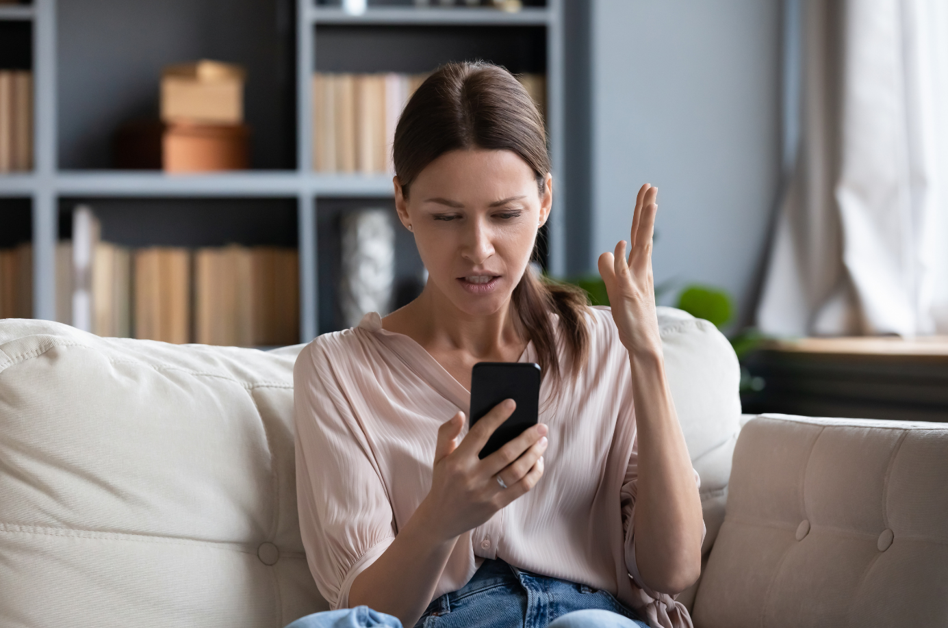 A frustrated woman looking at phone with an annoyed expression, depicting a long wait on a child support helpline.