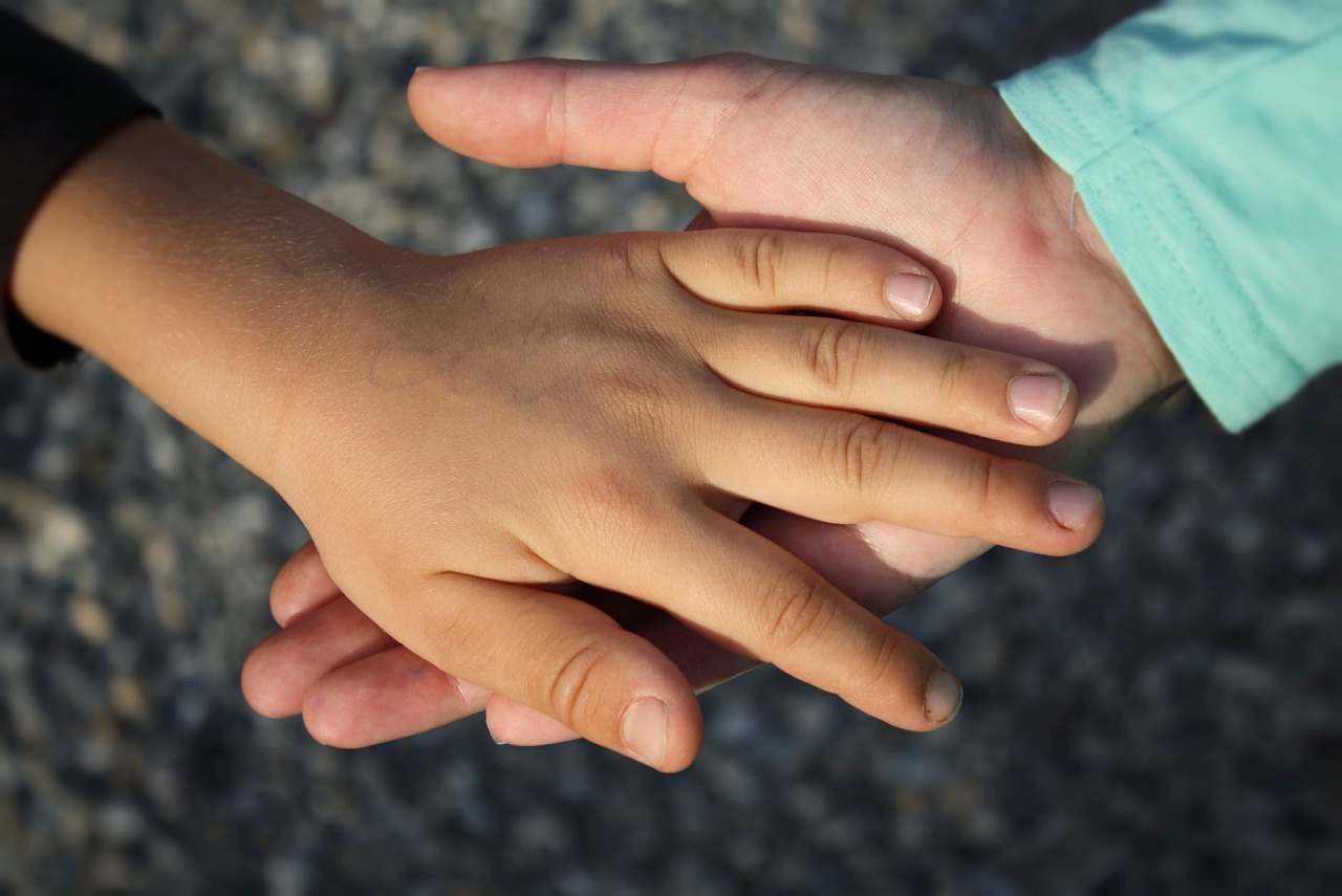 Adult holding a child's hand with blurred background.