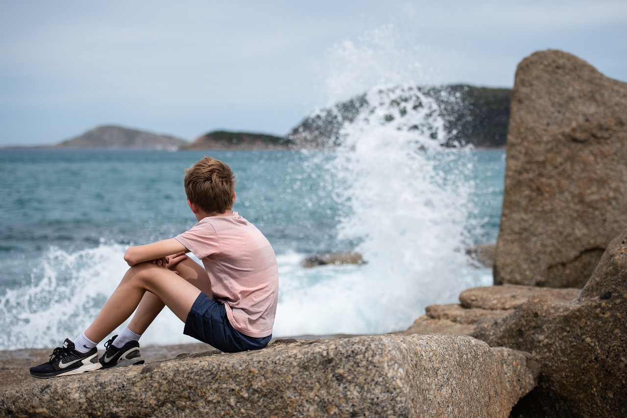 Child staring out at ocean as the waves crash on the rocks