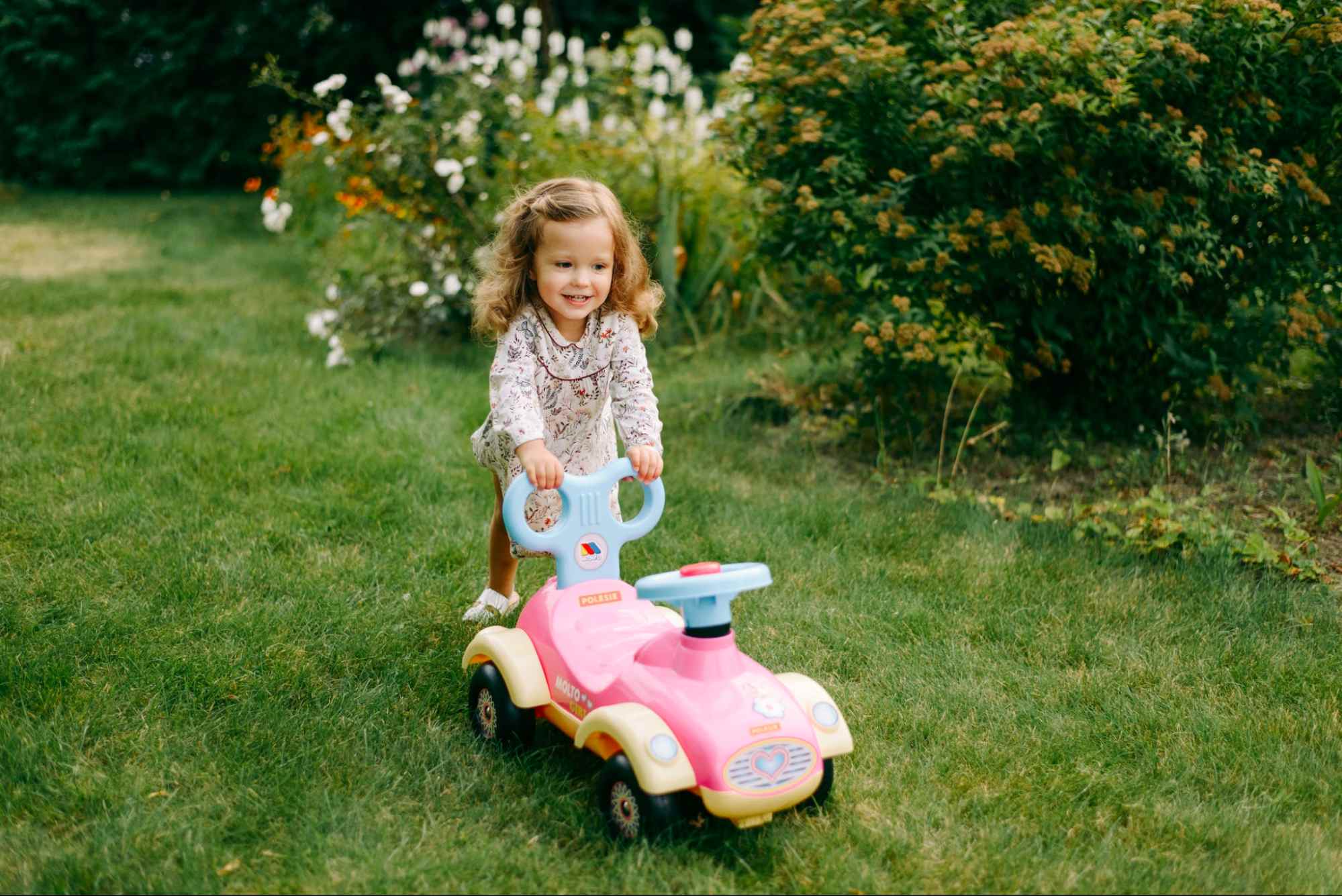 This is an image of a child pushing a toy car on the grass.