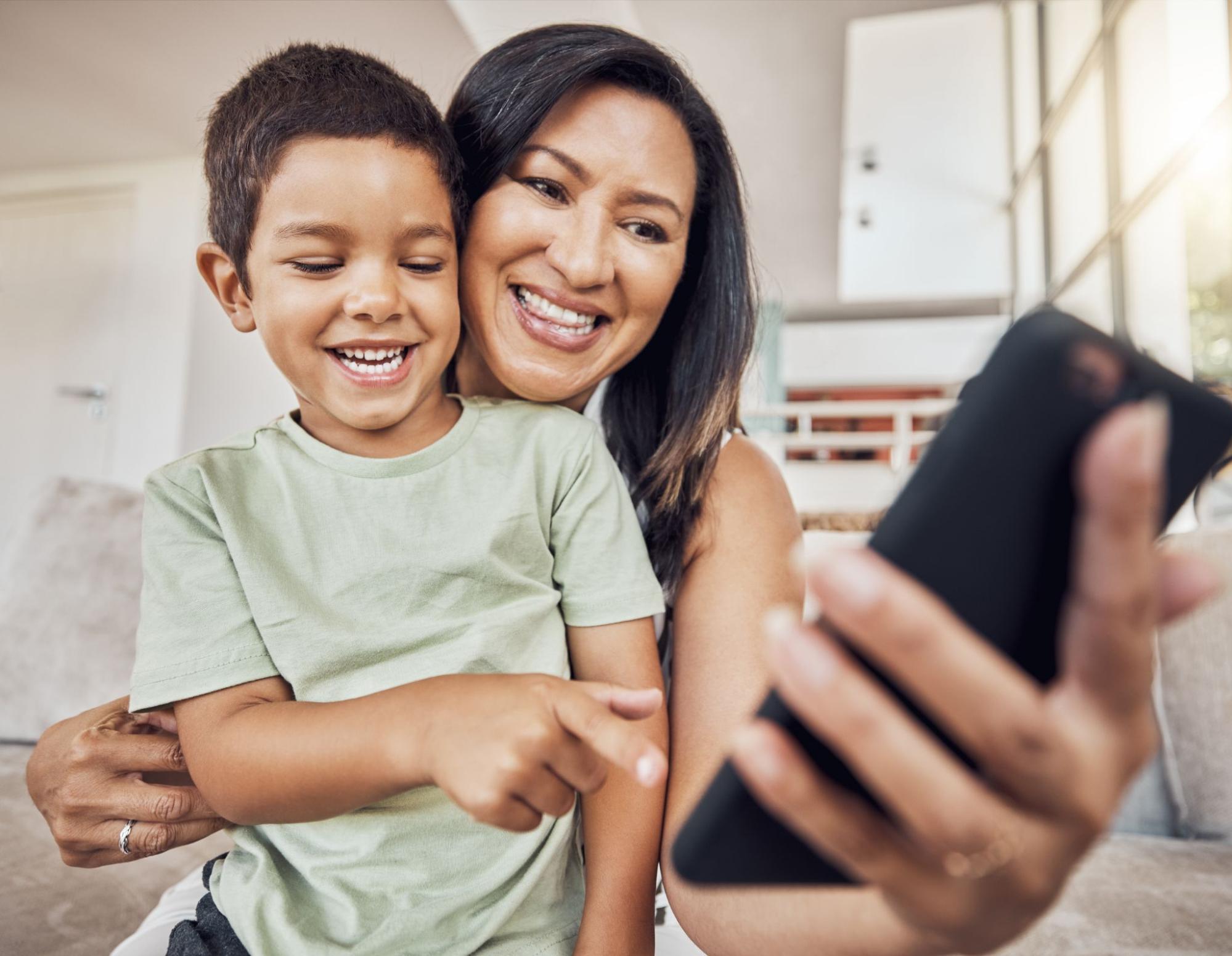A mother and her child are smiling as they look at a mobile phone.