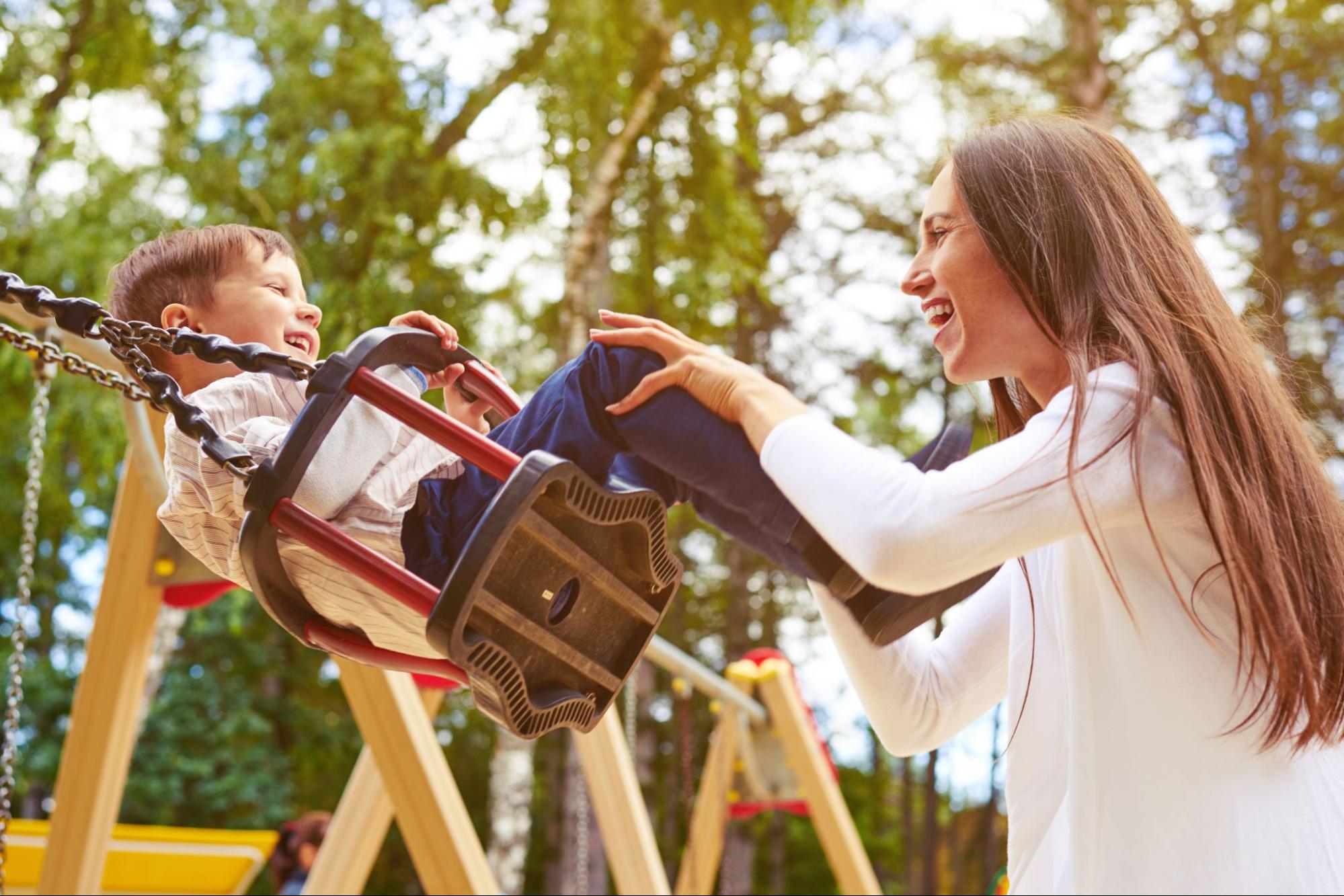 This is an image of a mother pushing her child on a playground swing.