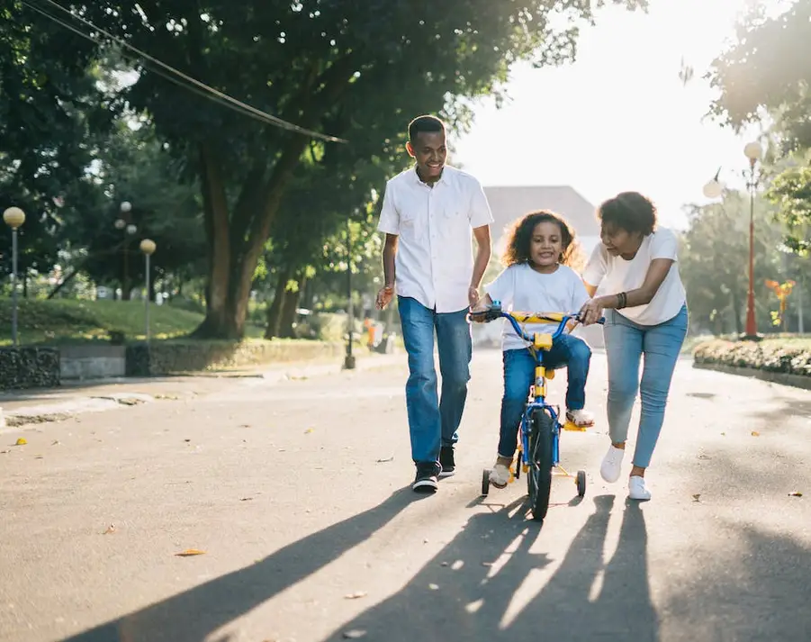 This is an image of two parents helping their child learn how to ride a bike.