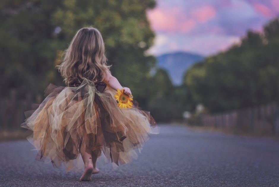 This is an image of a young girl in a dress, barefoot, strolling confidently down a laneway.