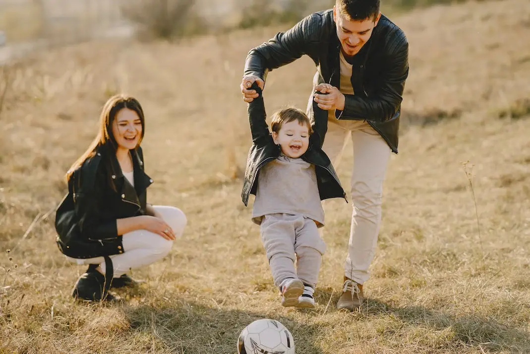 This is an image of two parents playing with their child and a soccer ball.