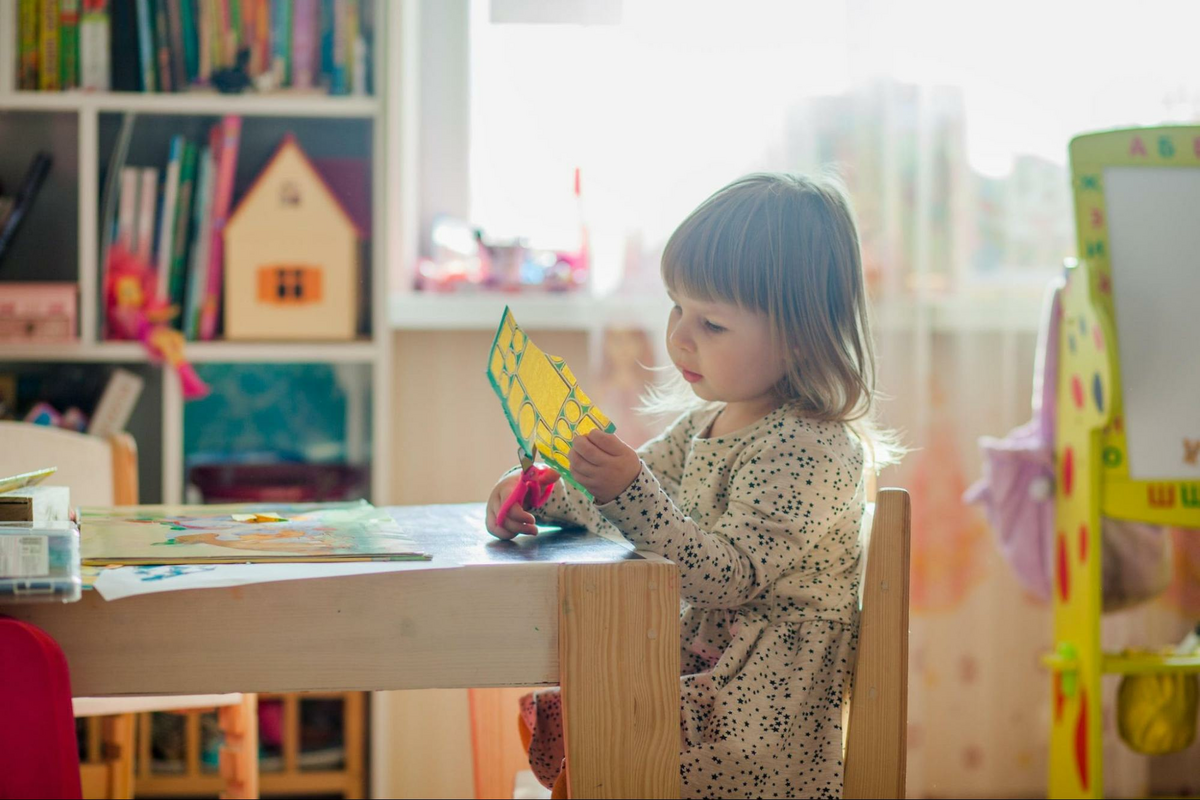 A child uses scissors to cut up a piece of paper in her playroom.