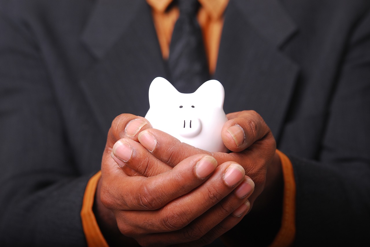 Man holding small, white piggy bank while wearing a suit