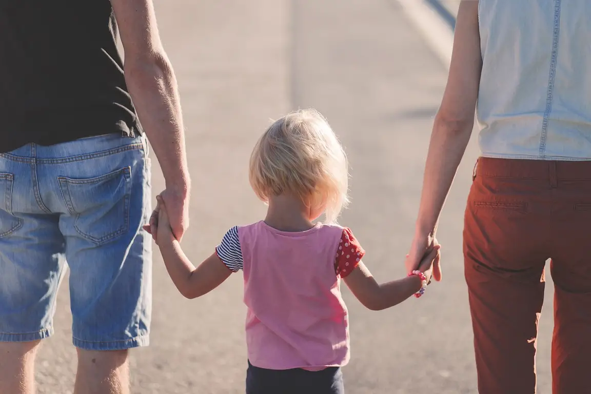 Child walking while holding hands with both parents.